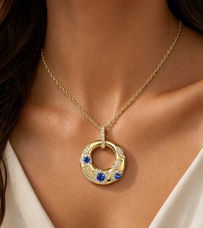 Gold necklace with a circular pendant featuring blue stones on a person wearing a white top.