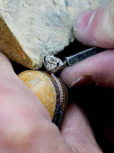 Close-up of bench jeweler holding a diamond ring with a stone background